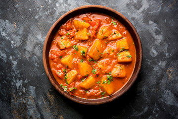Indian food - Aloo curry masala. Potato cooked with spices and herbs in a tomato curry. served in a bowl over moody background. selective focus