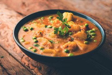 Indian Aloo Mutter curry - Potato and Peas immersed in an Onion Tomato Gravy and garnished with coriander leaves. Served in a Karahi/kadhai or pan or bowl. selective focus