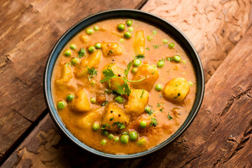 Indian Aloo Mutter curry - Potato and Peas immersed in an Onion Tomato Gravy and garnished with coriander leaves. Served in a Karahi/kadhai or pan or bowl. selective focus