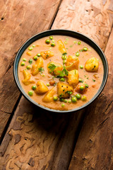 Indian Aloo Mutter curry - Potato and Peas immersed in an Onion Tomato Gravy and garnished with coriander leaves. Served in a Karahi/kadhai or pan or bowl. selective focus