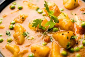 Indian Aloo Mutter curry - Potato and Peas immersed in an Onion Tomato Gravy and garnished with coriander leaves. Served in a Karahi/kadhai or pan or bowl. selective focus