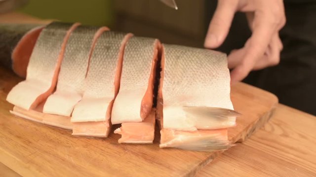 Close-up of female hands are cutting with a knife a large salmon on a wooden table of home cooking