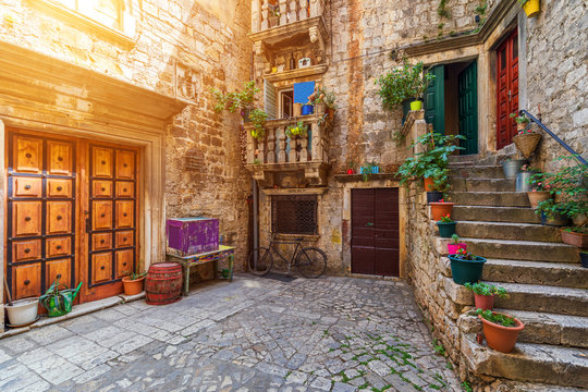 Fototapeta Narrow street in historic town Trogir, Croatia. Travel destination. Narrow old street in Trogir city, Croatia. The alleys of the old town of Trogir are very picturesque and full of charm. Croatia.
