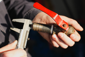 The worker holds in his hand a tap and a caliper. Measures the diameter of the pipe. Close-up