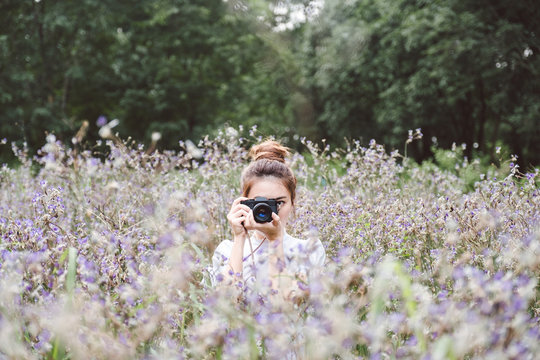 Woman with a camera the middle of the meadow with violet flowers Murdannia Giganteum in Prachinburi, Thailand. Photographer in nature. 