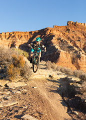 A woman wearing teal and grey rides a mountain bike down the Jem trail below Gooseberry mesa in the Southern Utah desert.