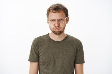 Fototapeta premium Man feeling mad of friends holding breath and pouting from offence and anger frowning swearing not say any word unless they sorry standing childish and displeased over grey wall in dark-green t-shirt