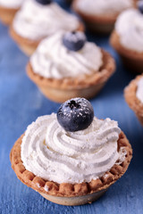 Bright tartlets filled with curd cream and decorated with blueberries on top are on a blue wooden desk, close up, vertical