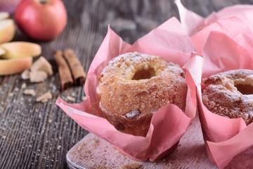 Appetizing, delicious muffins with apple and cinnamon in pink paper wrapper close to a whole ripe rose apple and slices of sliced ​​apple next to cinnamon sticks and sugar crumbs,  close up