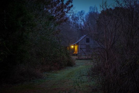 An old house in the distance in the country in the early morning twilight with the front porch light on. Belvidere, TN.