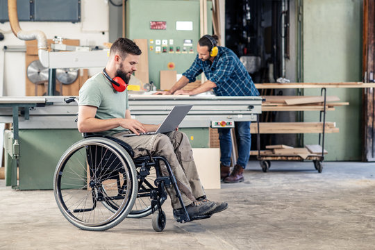 worker in wheelchair with computer in a carpenter's workshop with his colleagu