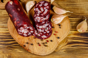 Sliced salami sausage on cutting board on wooden table. Top view