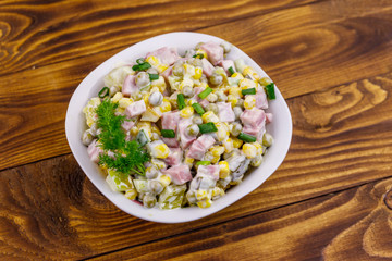 Tasty salad with sausage, green pea, canned corn, bell pepper, cucumber and mayonnaise on wooden table. Top view