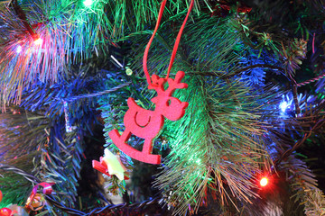 A close view of a green leaves Christmas tree with electric lights decorations, hanging ornaments and a red felt reindeer in a colored atmosphere