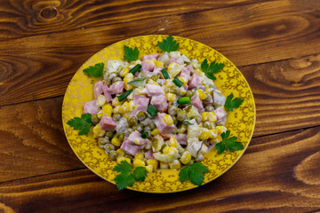 Tasty salad with sausage, green pea, canned corn, bell pepper, cucumber and mayonnaise on wooden table