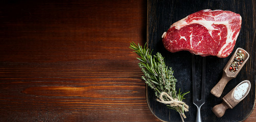 a piece of fresh marbled beef on a wooden background, with spices for cooking steak