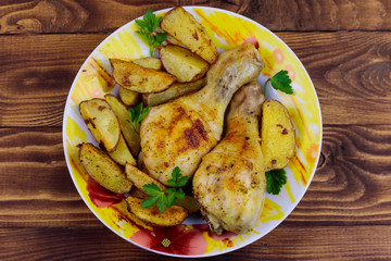 Baked chicken drumsticks with potatoes in a plate on wooden table