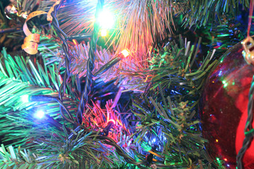 A close view of a green leaves Christmas tree with electric lights decorations and hanging ornaments in a bright colored atmosphere