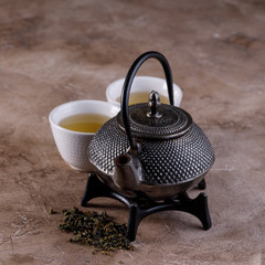 Obraz na płótnie Canvas Traditional Asian herbal tea, cooked in a cast-iron kettle with dry herbs and two tea bowls on a textured background. Close-up.