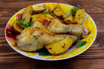 Baked chicken drumsticks with potatoes in a plate on wooden table