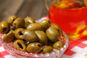 Olives with spices in a crystal bowl and pitcher with olive oil on dish towel. Old rustic wooden table.