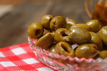 Olives with spices in a crystal bowl and pitcher with olive oil on dish towel. Old rustic wooden table.