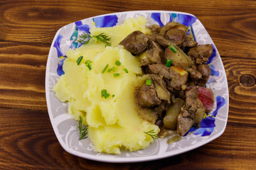 Mashed potatoes with stewed chicken liver with apple and onion on wooden table