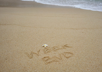 Week end written on wet sand with plumeria flower