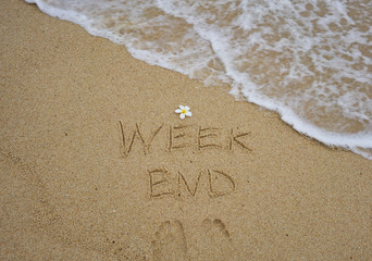 Week end written on wet sand with plumeria flower