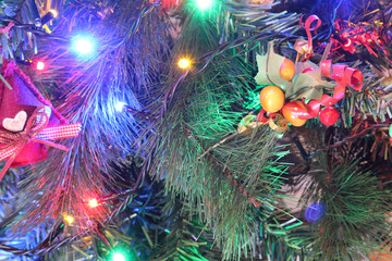A close view of a green leaves Christmas tree with electric lights decorations, hanging ornaments and red berries in a bright colored atmosphere