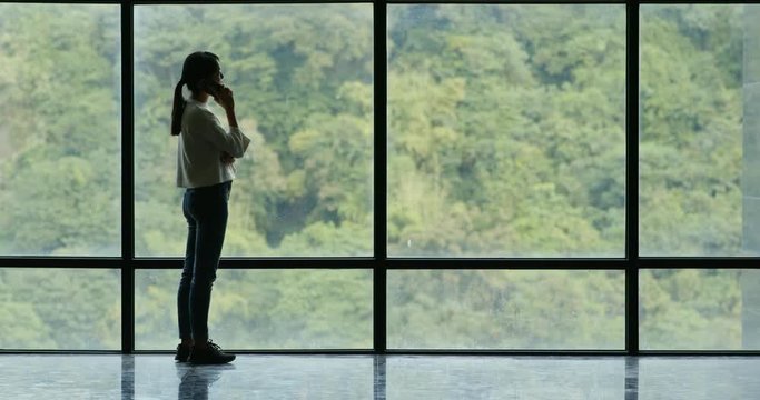 Woman talk to cellphone over glass of window with green tree background