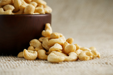 Cashew nuts in a wooden bowl on a burlap cloth background.