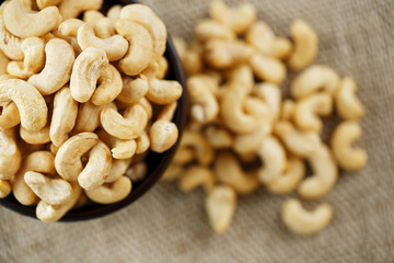 Cashew nuts in a wooden bowl on a burlap cloth background.