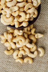 Cashew nuts in a wooden bowl on a burlap cloth background.