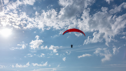 Red Glider in blue cloudy sky. The sun in the frame