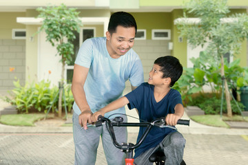 Asian little boy learns to ride a bike with his father