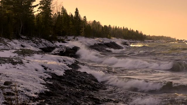 Rough winter waves breaking in later afternoon sunlight, approaching sunset on frozen winter shoreline, Lake Superior, Upper Peninsula, Michigan. 4K UHD