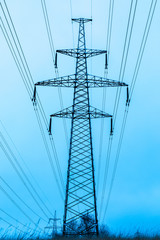 Towers of electric main in the winter snowy countryside field on the background of blue sky and the forest with the wires