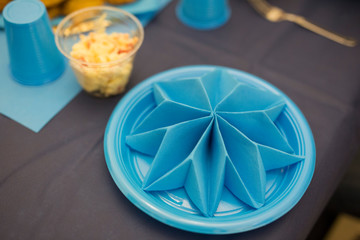 horizontal image with detail of a blue origami folded paper napkin on a blue plate