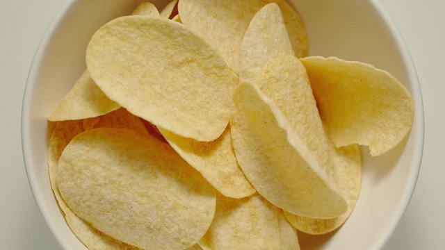 SLOW MOTION: Potato crisps falling into a white bowl - Top View