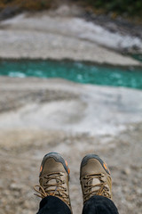 Fototapeta premium Shoes and serenity. Legs hanging with river flowing in the background