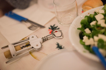 horizontal image with a close-up detail of a white corkscrew laid on a table during a lunch