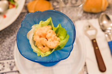horizontal image with close up detail of a prawn cocktail served in a blue glass cup during a party