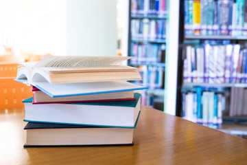 Open book stack on wood desk and blurred bookshelf in the library room.