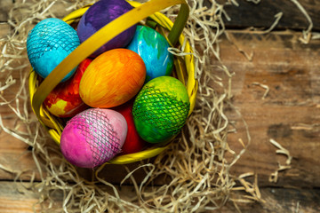 beautiful, bright, colorful hand-painted Easter eggs in a yellow basket on a natural, wooden background