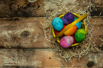 beautiful, bright, colorful hand-painted Easter eggs in a yellow basket on a natural, wooden background