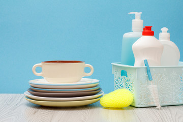 Bottles of dishwashing liquid in basket and plates on blue background.