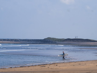 Fototapeta na wymiar Irland Urlaub Surfer mit Surfbrett am Strand