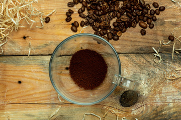 A glass cup with instant coffee next to roasted coffee beans, on a wooden, natural, rustic table