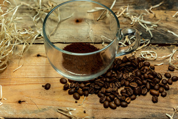 A glass cup with instant coffee next to roasted coffee beans, on a wooden, natural, rustic table